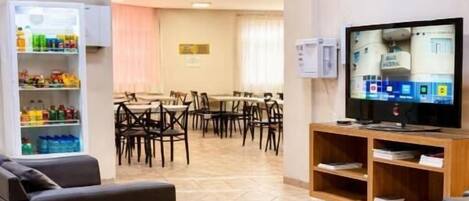 Un espacio de sala de estar con televisor, sofás, un refrigerador para bocadillos y un comedor con sillas y mesas.