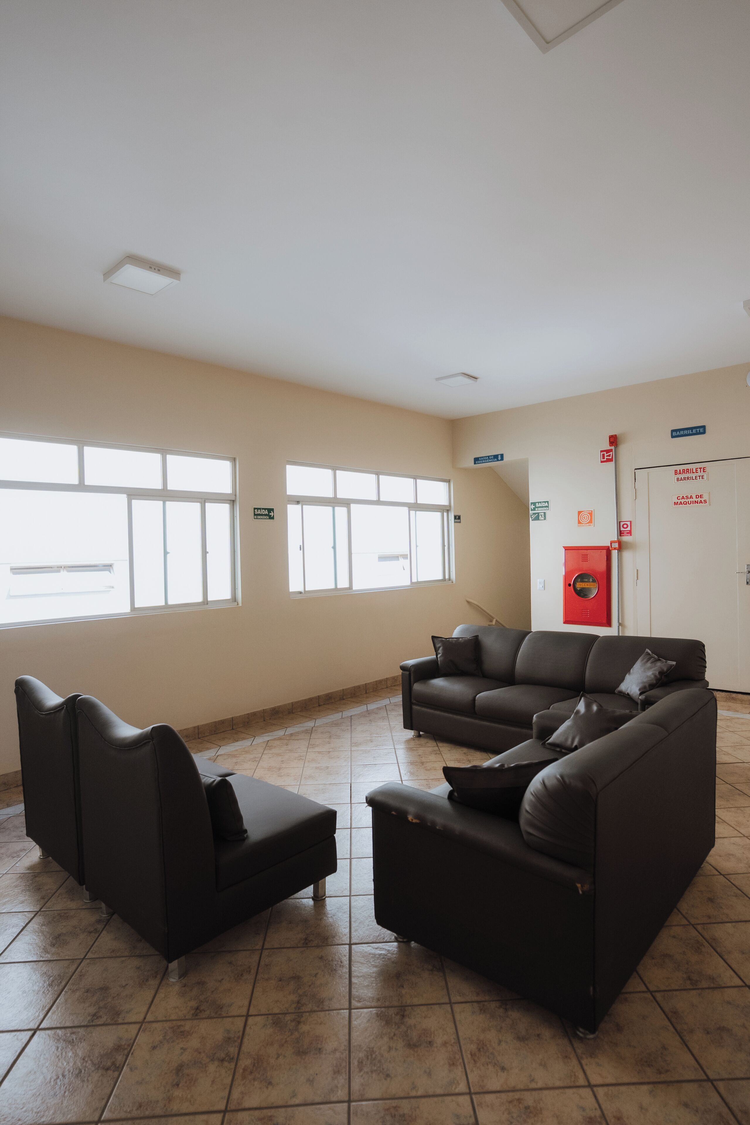 Una habitación amplia con un ventanal grande, un sofá, una silla y un letrero rojo de salida de emergencia.