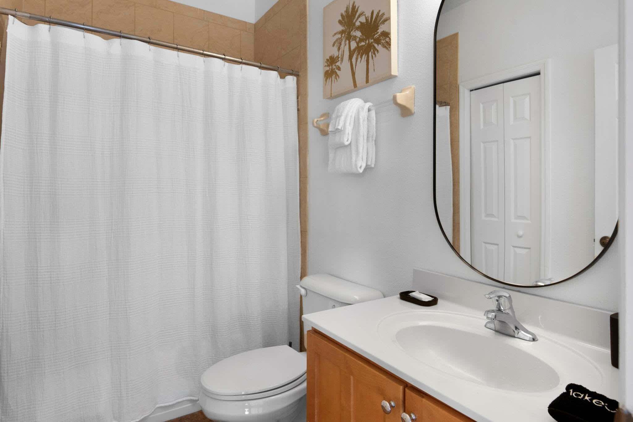 Une salle de bain équipée de toilettes, d’un lavabo, d’un miroir et d’un rideau de douche.