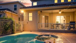 Ein Schwimmbad mit Whirlpool, eine überdachte Terrasse mit Gartenmöbeln und ein umzäunter Gartenbereich.