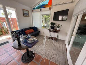 Ein gemütlicher Wohnbereich mit einer Couch, einem Esstisch mit Stühlen, einem an der Wand befestigten Fernseher und einem Fenster mit Jalousien.