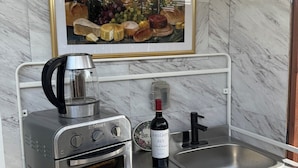 Una cocina con horno empotrado, cafetera, una botella de vino y un cuadro enmarcado sobre la encimera.