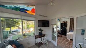 Una sala de estar con un sofá, una mesa de comedor con sillas, un televisor montado en la pared y vistas al exterior.