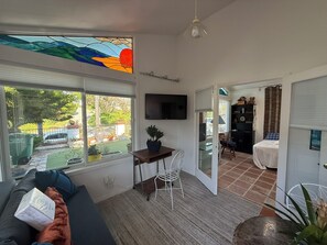 Ein Wohnzimmer mit einer Couch, einem Esstisch mit Stühlen, einem an der Wand befestigten Fernseher und Blick ins Freie.