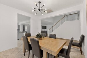 A dining area with a wooden table, six chairs, a chandelier, and a staircase in the background. - Large 6BR 3BA Home Near AT&T Stadium & Six Flags (Grand Prairie)