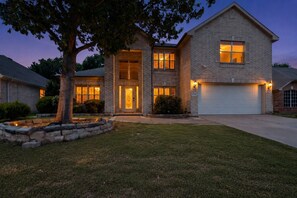 A two-story house with a garage, a well-maintained lawn, and a tree in the front yard. - Large 6BR 3BA Home Near AT&T Stadium & Six Flags (Grand Prairie)