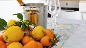 Une cuisine avec un panier de fruits contenant des citrons et des oranges, un verre de jus d’orange et un verre à vin.