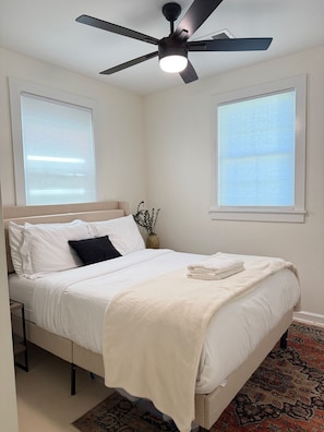 A bedroom with a bed, a ceiling fan, a window, and a nightstand.
