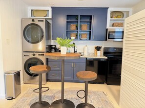 A compact kitchen with a washing machine, a microwave, a dishwasher, and a small dining area with stools.