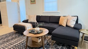 Ein modernes Wohnzimmer mit einem schwarzen Ecksofa, einem runden Couchtisch aus Holz und einem gemusterten Teppich.