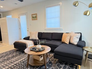 A modern living room with a black sectional sofa, a round wooden coffee table, and a patterned rug.