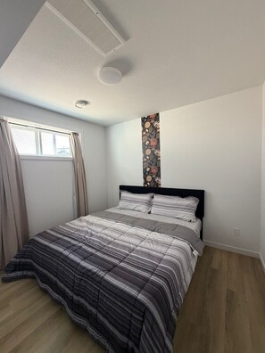 Ein Schlafzimmer mit Bett, einem fensterbelaubten Fenster, einem Wandlüfter und einer Wandtapete mit Muster.