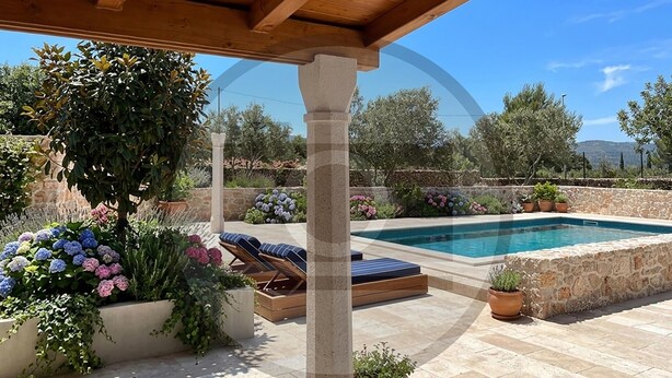 Un área de piscina con muros de piedra, sillones reclinables y plantas en macetas.