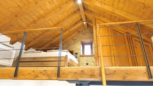 Un dormitorio tipo loft con techo inclinado, vigas de madera y un ventanal pequeño.