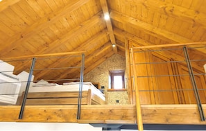 Ein Schlafzimmer im Loft-Stil mit schrägem Dach, Holzbalken und einem kleinen Fenster.