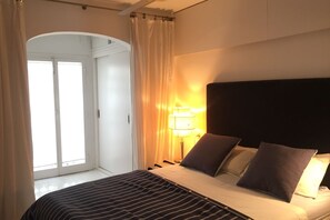 Ein Schlafzimmer mit Bett, Vorhängen, einer Lampe und Blick auf eine Tür.