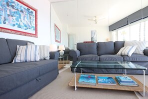 Ein modernes Wohnzimmer mit einem grauen Sofa, einem Glastisch und Büchern darauf.