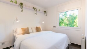 Une chambre à coucher avec un lit, des lampes de chevet, une fenêtre et des plantes suspendues.