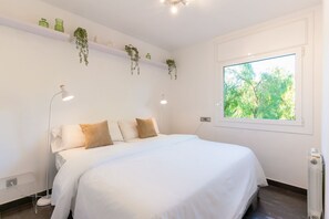 Ein Schlafzimmer mit Bett, Nachttischlampen, einem Fenster und hängenden Pflanzen.