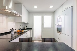 A modern kitchen with white cabinets, a black countertop, a coffee maker, and a window. - Apartment Lily I - Three Bedroom Apartment, Sleeps 7 (Sitges)