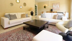 Una sala de estar con dos sofás blancos, una mesa de centro oscura y una alfombra estampada.