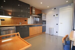 A modern kitchen with a dishwasher, oven, and microwave. There is a wooden dining table with chairs. - Apartment Parc Del Mar (Sitges)