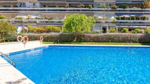 Una piscina con superficie de agua azul cristalina, rodeada por un seto cuidado y árboles.