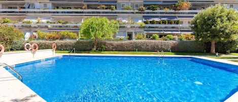 A swimming pool with a clear blue water surface, surrounded by a well-maintained hedge and trees.