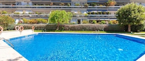 A swimming pool with a clear blue water surface, surrounded by a well-maintained hedge and trees. - Apartment Parc Del Mar (Sitges)