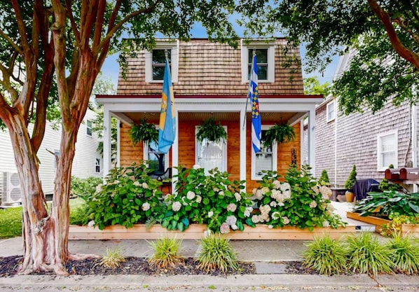 A two-story house with a front porch, wooden siding, and a small garden with hydrangeas.