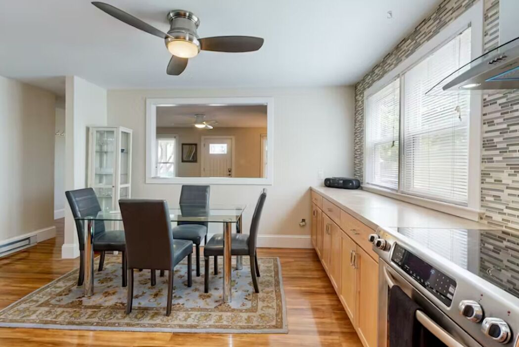 A dining area with a glass table and chairs, a ceiling fan, and a kitchen with a stove and oven.