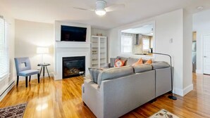 Un salon avec un canapé gris, une cheminée, un ventilateur de plafond et un téléviseur fixé au-dessus de la cheminée.
