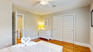 Une chambre à coucher avec un lit, une commode blanche, un ventilateur de plafond et une porte.