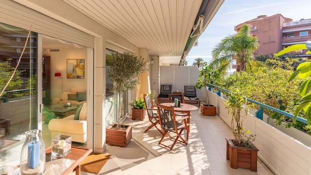 A balcony with a sofa, a table, and chairs, surrounded by potted plants. - Apartment Terramar - Four Bedroom Apartment, Sleeps 8 (Sitges)