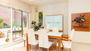A dining area with a glass partition, a wooden table, white chairs, and a potted plant. - Apartment Terramar - Four Bedroom Apartment, Sleeps 8 (Sitges)