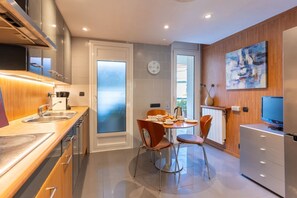 A modern kitchen with a dining area, stainless steel appliances, and a wooden accent wall. - Apartment Terramar - Four Bedroom Apartment, Sleeps 8 (Sitges)