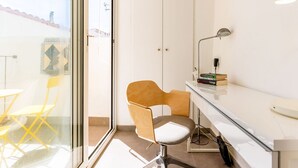 A modern room with a glass door leading to a balcony, a wooden chair, a desk with a lamp, and a small bookshelf. - Casa Cipres - Three Bedroom Apartment, Sleeps 6 (Sitges)