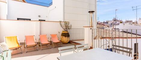Eine Dachterrasse mit Tisch und Stühlen, einer Topfpflanze und Blick auf die Stadtlandschaft.