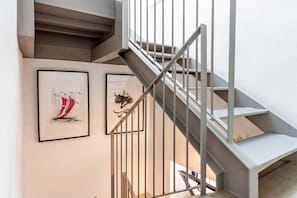 Un escalier avec des rampes en métal et un mur blanc orné de deux œuvres d’art encadrées.