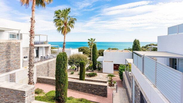 Un quartier résidentiel moderne offrant une vue sur la mer, avec des murs en pierre et des palmiers.