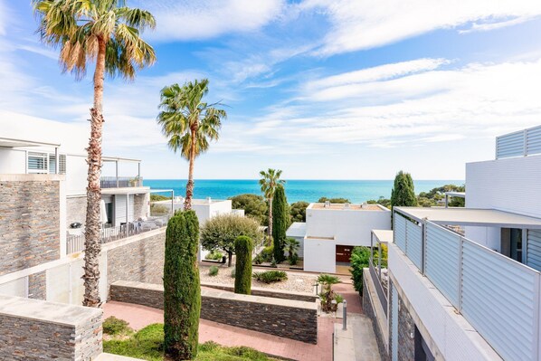 A modern residential area with a view of the sea, stone walls, and palm trees. - Casa Del Mar - Three Bedroom Apartment, Sleeps 6 (Sant Pere de Ribes)
