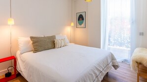 Une chambre à coucher avec un lit, des lampes de chevet, un tableau encadré et une fenêtre avec des rideaux.