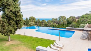 Une piscine avec vue sur la mer, entourée d’une pelouse et d’arbres.