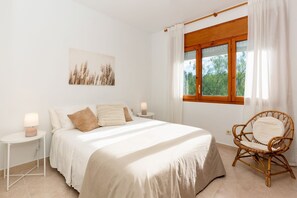 Ein Schlafzimmer mit einem Bett, Nachttischen, einem Sessel, einem Fenster mit Vorhängen und einem Wandbild.