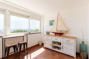 Ein Zimmer mit großem Fenster, einem Segelbootmodell, zwei Hocker, einem Schrank und einer Vase.