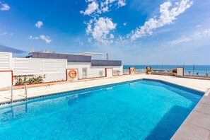 Ein klares, blaues Schwimmbecken mit Blick auf das Meer, einem Rettungsring und einem weißen Gebäude mit einem Rettungsschwimmturm.