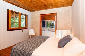A bedroom with a wooden ceiling, a bed with a striped blanket, a white chair, and a window with a view of greenery. - Casa Mokki - Three Bedroom Villa, Sleeps 7 (Olèrdola)