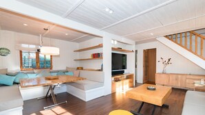 En moderne stue med sofa, spisebord, fjernsyn og trappe.
