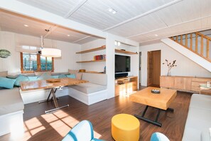 A modern living room with a sofa, a dining table, a TV, and a staircase. - Casa Mokki - Three Bedroom Villa, Sleeps 7 (Olèrdola)
