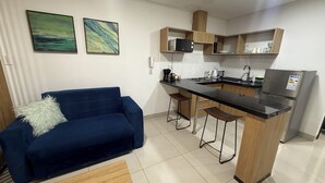 Una cucina compatta con un divano blu, due sgabelli, un frigorifero e un forno a microonde.